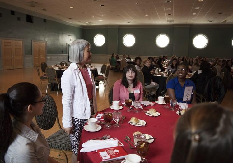 woman standing by table, others listening